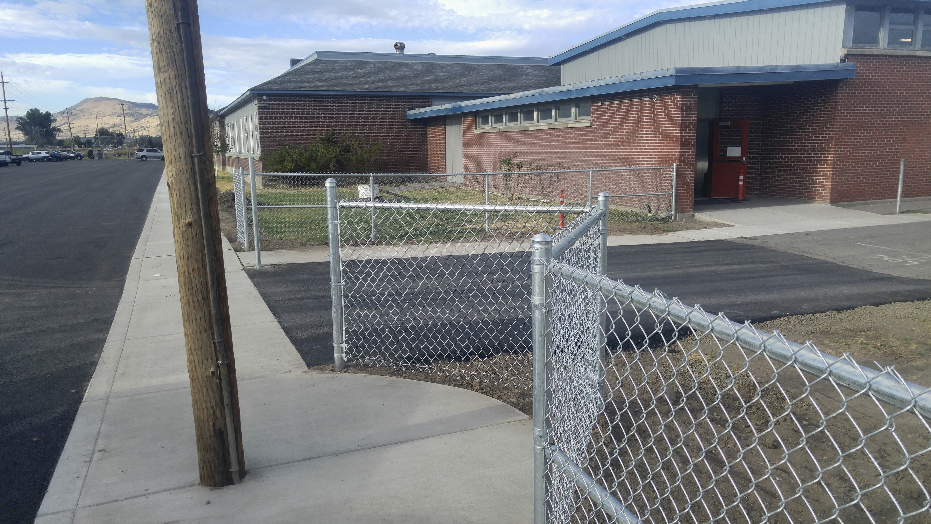 New galvanized chain link fence installed along a brick school building — Klamath Falls, OR
