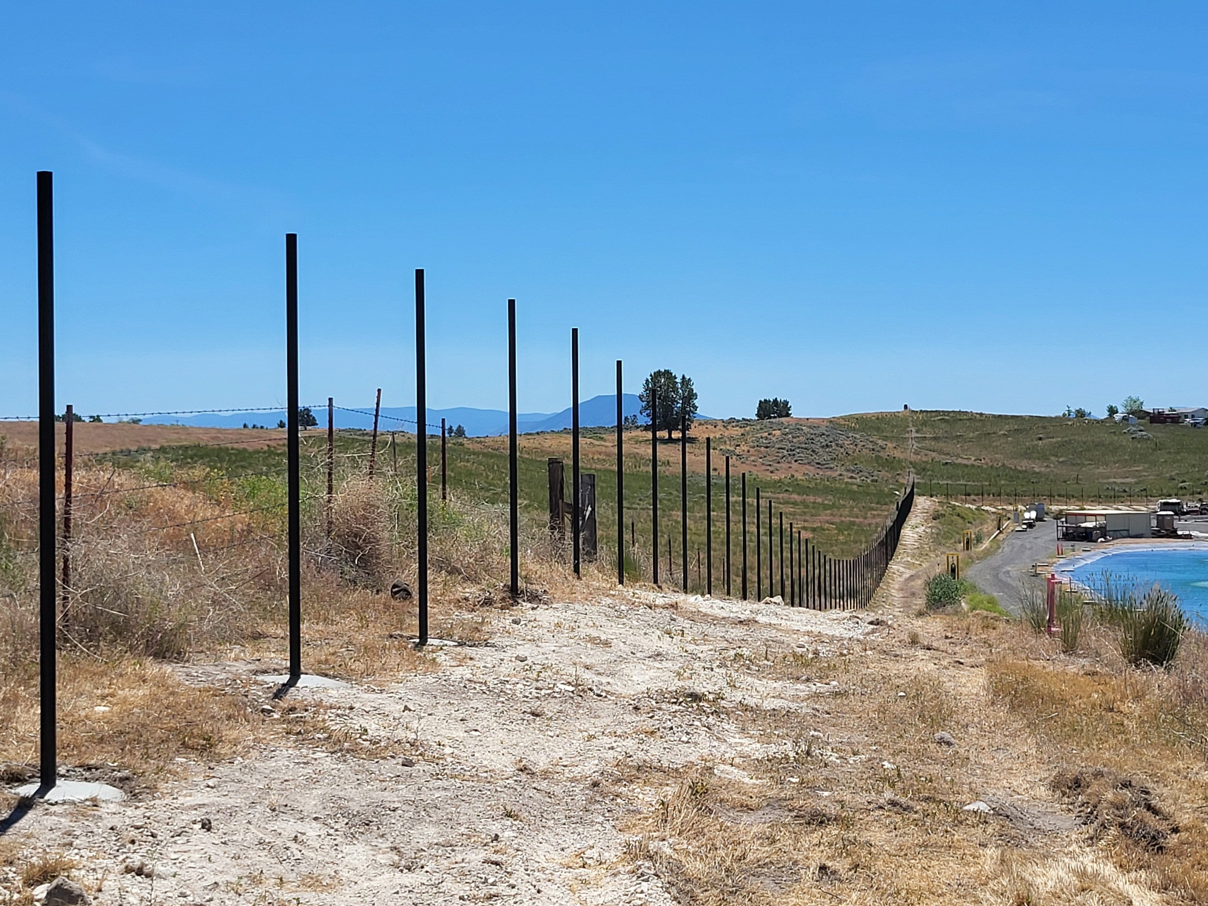 Steel post fence installation on a rolling hillside with mountain views